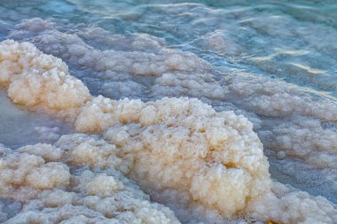 Dead Sea coastline with natural salt crystals at sunset. Texture of Dead sea in Ein Bokek, Israel. Waterscape of Salty seashore. Crystalline salt natural mineral formation at the on beach of Dead-Sea.