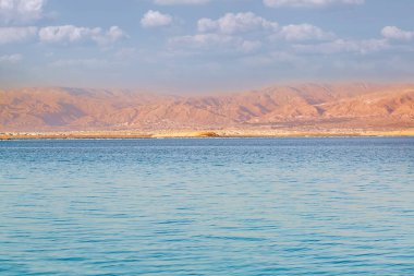 Evening sun shines on salt crystals formations, clear blue water near. Picture at Dead Sea beach in Ein Bokek, Israel. Waterscape of seashore. Sea season summer during fantastic dawn. Lowest elevation