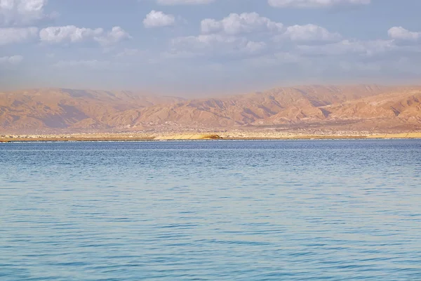 Evening sun shines on salt crystals formations, clear blue water near. Picture at Dead Sea beach in Ein Bokek, Israel. Waterscape of seashore. Sea season summer during fantastic dawn. Lowest elevation