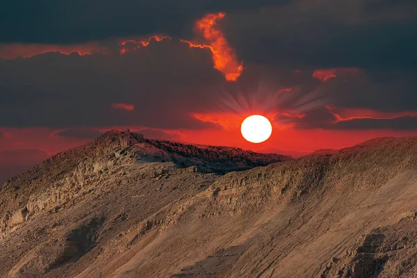 Dramatic evening red sunset sky over mountain Sodom Gomorrah in Dead sea from Negev desert, Israel.  Sunset on a foggy mountains range Sodom with fluffy clouds. Sun shining on rocky landscape in hills