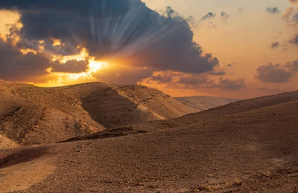 Sunset in the desert and sun rays spreading. Beautiful dramatic clouds on gold sky. Golden sand dunes in desert in Judean desert, Israel. Sunny sky over cliffs, large salt mountains Sodom and Gomorrah