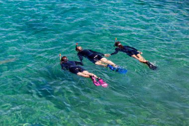 Dalış maskeleri ve paletleriyle üç kadın dalgıç Eilat, Kızıl Deniz, İsrail 'de kristal berrak suya dalıyorlar. Dalgıçlar denizde antrenman yapıyor. Suda oynayan siyah dalış takımlı genç kız dalgıç.