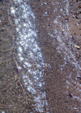 Yukarıdan taşlı bir deniz tabanına, deniz yüzeyindeki kristal berrak suya bak. Yukarıdan görülen deniz tabanının genel görünümü, şeffaf köpüklü su güneş ışığını yansıtır. Fotoğraf filtresiyle çekilmiş.