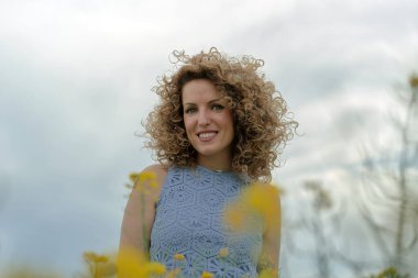 Öndeki genç kız, kıvırcık saçları ve mavi gözleriyle kameraya bakıyor..