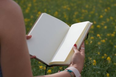 hands of a girl grabbing a white notepad in the field