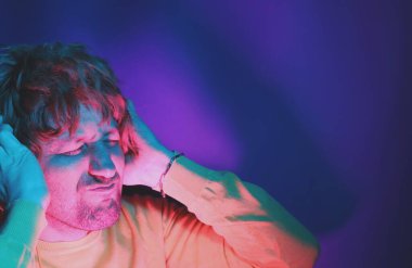 Young expressing man in wireless headphones and listening to his favourite song, dancing, smiling with closed eyes. Violet background.