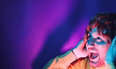 Happy hipster man listening music with headphones at black studio with neon lights. Disco, night club, hip hop style, positive emotions, face expression, dancing concept.