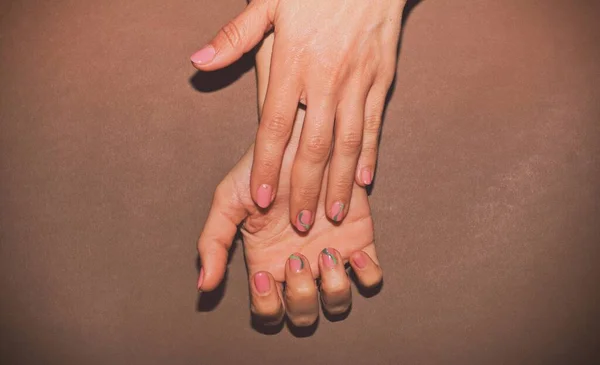 Hands of a beautiful well-groomed woman with feminine nails on a brown background. Manicure, pedicure beauty salon concept. Empty space for text or logo. On nails white gel polish