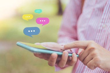 Açık doğa parkı arka planında sohbet ikonu olan akıllı bir telefon kullanarak kadın el ele tutuşunu kapat. Teknoloji ve seyahat tatil konseptinin kopyalama alanı. Klasik ton filtre efekti rengi.