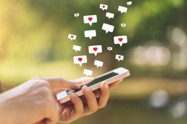 Açık hava parkı arka planında kalp ikonu olan akıllı bir telefon kullanarak kadının elini tutun. Teknoloji ve seyahat tatil konseptinin kopyalama alanı. Klasik ton filtre efekti renk biçimi.
