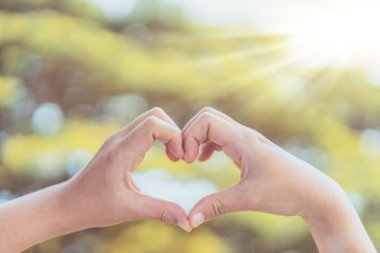 Doğada kadın eli kalp şekli Bokeh güneş ışığı parıltısı ve bulanık yaprak soyut arka plan. Mutlu aşk ve özgürlük kavramını kopyala. Klasik ton filtresi renk biçimi.