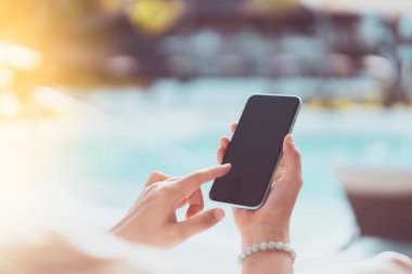 Akıllı telefon kullanan ve yüzme havuzunda yatağında oturan bir kadın. Teknoloji işi ve seyahat tatili konsepti. Klasik ton filtre efekti renk biçimi.