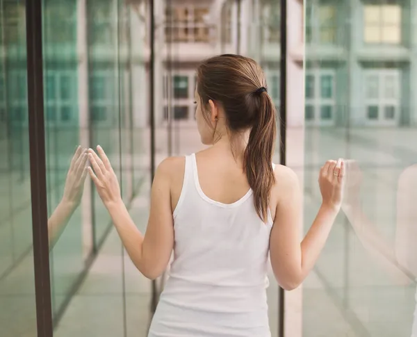 Toned picture of a young girl viewed from the back standing between the glass walls. — Stock Photo, Image