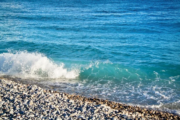 Azure sea waves. Clear blue water with white foam. Pebbles on th — Stock Photo, Image