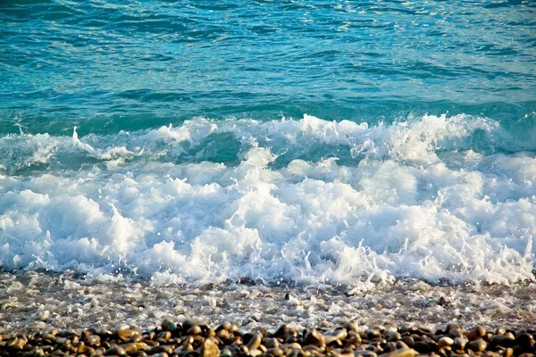 Azure sea waves. Clear blue water with white foam. Pebbles on th — Stock Photo, Image