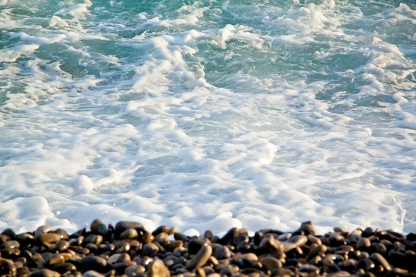 Azure sea waves. Clear blue water with white foam. Pebbles on th — Stock Photo, Image