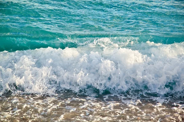 Azure sea waves. Clear blue water with white foam. Pebbles on th — Stock Photo, Image