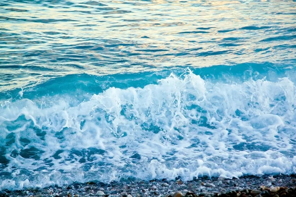 Azure sea waves. Clear blue water with white foam. Pebbles on th — Stock Photo, Image