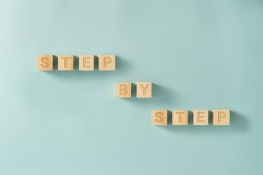 Mavi arkaplandaki tahta küplerde STEP sözcükleriyle adım, bloklar tarafından imzalanır