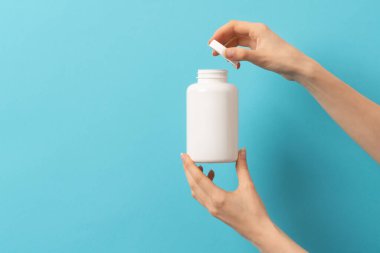 Mavi arka planda elinde ilaç şişesi tutan bir kadın.