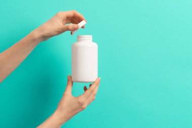 Beyaz ilaç şişesi ya da vitamin hapı ya da yeşil ve turkuaz arka plan takviyesi tutan kadın eli.