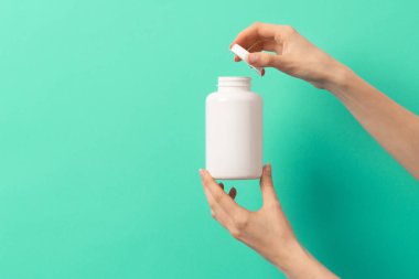 Beyaz ilaç şişesi ya da vitamin hapı ya da yeşil ve turkuaz arka plan takviyesi tutan kadın eli.