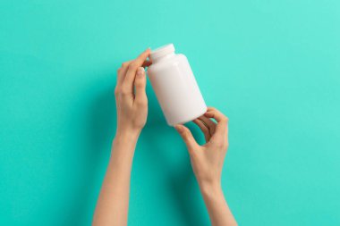 Beyaz ilaç şişesi ya da vitamin hapı ya da yeşil ve turkuaz arka plan takviyesi tutan kadın eli.