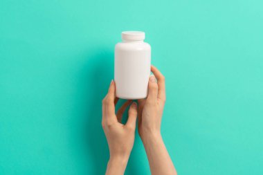Beyaz ilaç şişesi ya da vitamin hapı ya da yeşil ve turkuaz arka plan takviyesi tutan kadın eli.