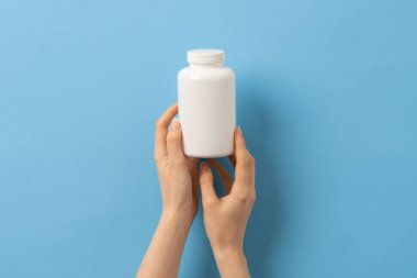 Mavi arka planda elinde ilaç şişesi tutan bir kadın.