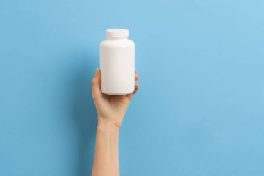 Mavi arka planda elinde ilaç şişesi tutan bir kadın.