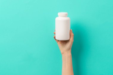 Beyaz ilaç şişesi ya da vitamin hapı ya da yeşil ve turkuaz arka plan takviyesi tutan kadın eli.
