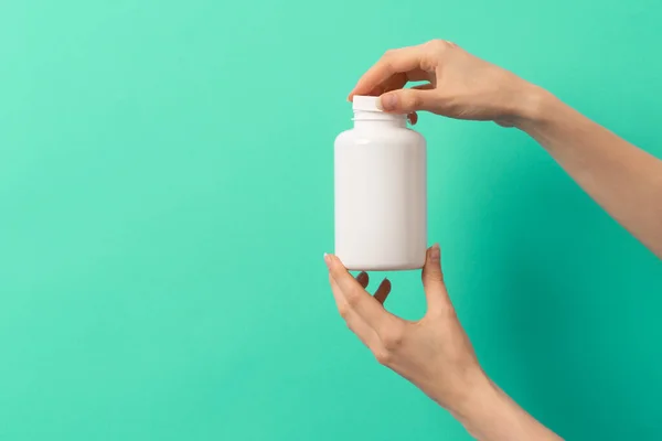 Beyaz ilaç şişesi ya da vitamin hapı ya da yeşil ve turkuaz arka plan takviyesi tutan kadın eli.