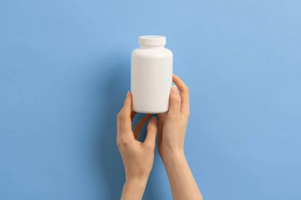 Mavi arka planda beyaz ilaç şişesi ya da vitamin ya da takviye malzemesi tutan bir kadın.