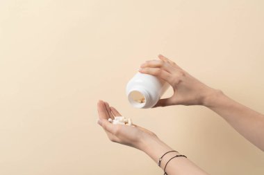 Beyaz hapların üzerine dökülen bir kadın ya da arka planda avucundaki vitaminler
