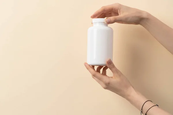 Bej arka planda bir şişe ilaç ya da vitamin tutan kadın eli