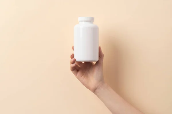Bej arka planda bir şişe ilaç ya da vitamin tutan kadın eli