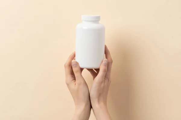 Bej arka planda bir şişe ilaç ya da vitamin tutan kadın eli