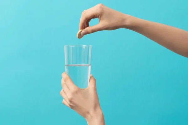 a female hand drops an effervescent tablet into the glass of water on the blue background