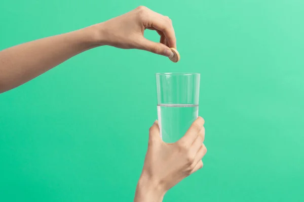 a female hand drops an effervescent tablet into the glass of water on the blue background