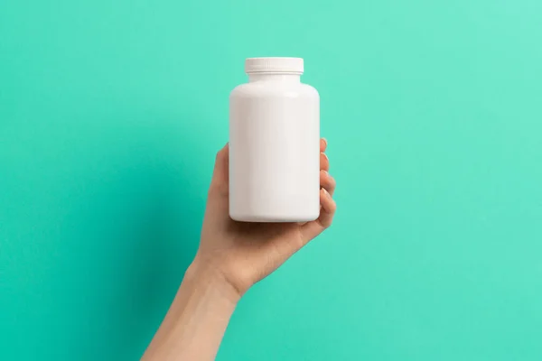 Beyaz ilaç şişesi ya da vitamin hapı ya da yeşil ve turkuaz arka plan takviyesi tutan kadın eli.