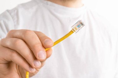 Adamın eli beyaz arka planda sarı kabloyu tutuyor. Kablosuz bağlantı yerine bilgisayarı internete bağlamaya çalışıyor.