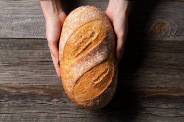 Bayan fırıncı taze pişmiş beyaz ekmeği eski ahşap masanın üstünde tutuyor..