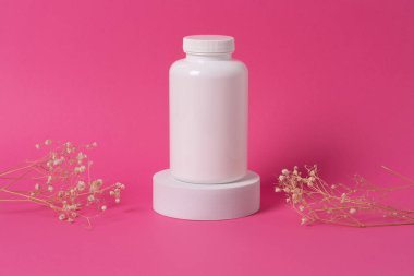 Beyaz ilaç şişesi. Ürün sunumu için etiketi boş. Pembe arka planda beyaz podyuma yerleştirilmiş..