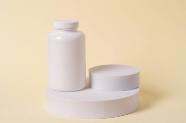 Renkli arka plandaki geometrik figürlere boş etiketli beyaz ilaç şişesi. Ürün yerleştirme için estetik bileşim.