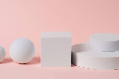 Açık pembe fırına yerleştirilmiş geometrik beyaz figürler. Kozmetik sunum için sergi.