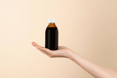 Masa kaşığı ve ilaç şişesiyle el resmi. Öksürük şurubu ya da soğuk algınlığı ilacını kaşığa dökmek. Etiketsiz şişe.