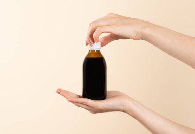 Kahverengi bir şişe soğuk algınlığı ilacı tutan eller. Ürün yerleştirme veya ürün sunumu için etiketsiz şişe. Bej arkaplan.