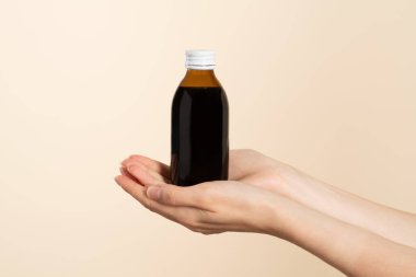 Kahverengi bir şişe soğuk algınlığı ilacı tutan eller. Ürün yerleştirme veya ürün sunumu için etiketsiz şişe. Bej arkaplan.