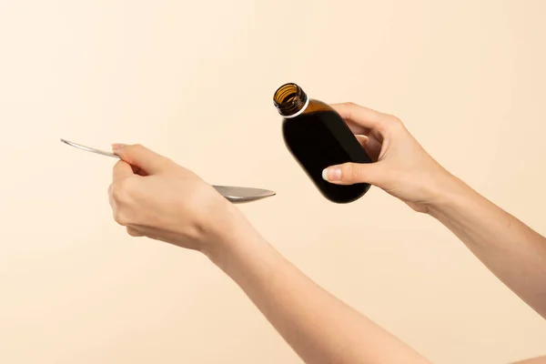 Image of hands with table spoon and bottle of medication. Pouring cough syrup or cold liquid medication into spoon. Bottle with no label.