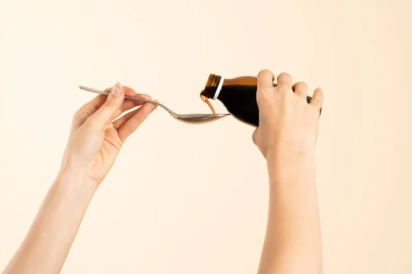 Image of hands with table spoon and bottle of medication. Pouring cough syrup or cold liquid medication into spoon. Bottle with no label.